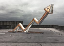 A shiney arrow made from chrome or steel sits on a car park pointing upwards