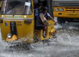 School children travelling in an auto rickshaw gesture as they are driven past a waterlogged street during a monsoon rainfall in Hyderabad, India.