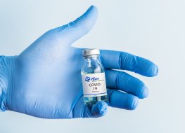 Gloved hand holding a vial of Pfizer's coronavirus vaccine. Photo source: Shutterstock_1898586559 