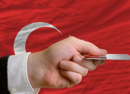 man stretching out credit card to buy goods in front of complete wavy national flag of turkey