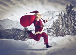 A person dressed like Santa Claus running outside in the snow with trees in the background