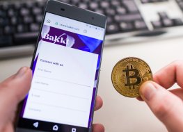 A customer holds a smartphone with a Bakkt Holdings logo in one hand a bitcoin token in the other