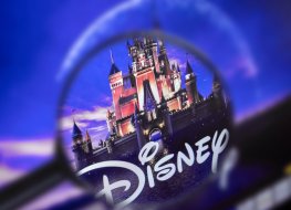 Disney stock forecast (2022–2025): Will the stock crash like Netflix? The home page of the Disney site, view through a magnifying glass. Disney company logo is visible. Soft focus.