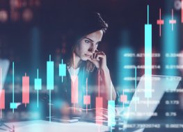 A female trader looking at a computer screen. Candle charts going up and down overlaid. 