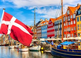 The famous view of Copenhagen. The famous old port of Nyhavn in the center of Copenhagen, Denmark, on a sunny summer day with the flag of Denmark in the foreground.