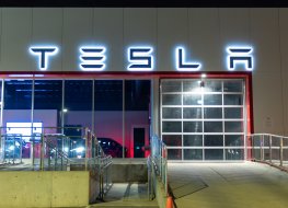 Tesla logo atop of a Tesla Dealership illuminated at night.