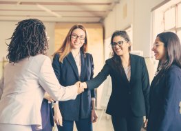 Smiling young businesswomen shaking hands in office. Confident cheerful business partners greeting each other.