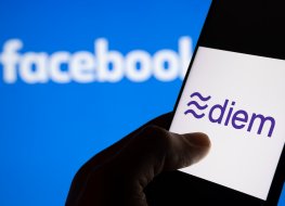 A hand holding phone with diem logo on a display against blue backround with Facebook logo.