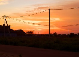 Rural landscape at sunset. Setting sun, houses, road and electrical line on bright orange sky background