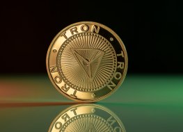 Tron price prediction. Tron TRX cryptocurrency physical coin placed on reflective surface and lit with green and red lights