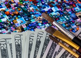 A picture of money with brushes placed on tablet screen showing Beeple NFT art collage Everydays – The First 5000 Days