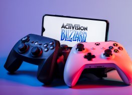 A smartphone with the Activision Blizzard logo on the screen on the pile of the gamepads
