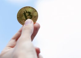 A human hand holding a golden coin with a bitcoin (BTC) logo.