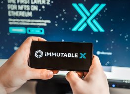 Man playing with crypto coins on a smartphone with the Immutable X logo in the background on a computer screen