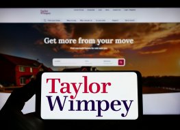 Stuttgart, Germany - 02-26-2022: Person holding smartphone with logo of British housebuilding company Taylor Wimpey plc on screen in front of website. Focus on phone display. Unmodified photo.