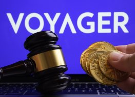 Voyager coins held in a male hand over a computer keyboard. Voyager logo in the background. A gavel on the side symbolising Voyager’s court hearings.