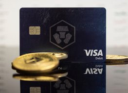 Cryptocurrency tokens lie on a table in front of a Crypto.com Visa card