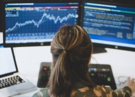A female trader looking at two screens displaying stock market data.
