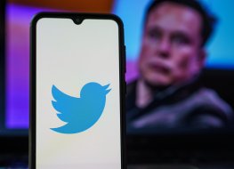 Twitter logo on cell phone with Elon Musk in the background.