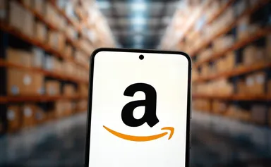 Amazon logo displayed on a smartphone screen with a blurred warehouse background