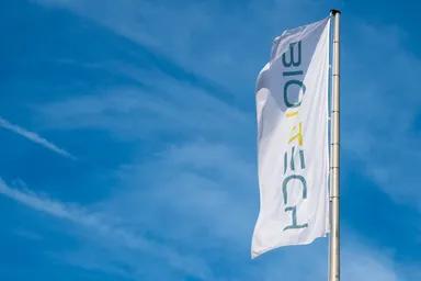 BioNTech-Flagge auf hohem Mast weht vor blauem Himmel mit leichten Wolken