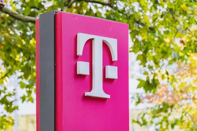 Deutsche Telekom logo on a pink sign outdoors with green trees in the background