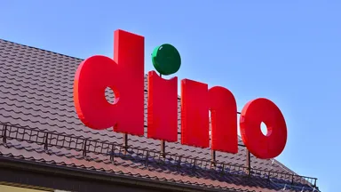 Logo supermarketu Dino umieszczone na dachu na tle czystego błękitnego nieba