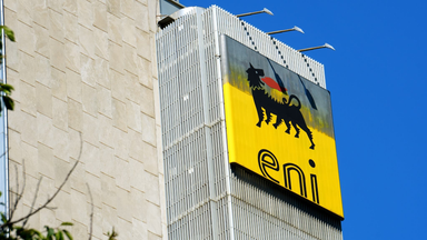 Eni logo on a yellow sign mounted on a modern office building against a clear blue sky