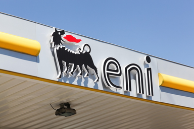 Logo Eni con il simbolo del cane a sei zampe esposto all'esterno di una stazione di servizio sotto un cielo azzurro.