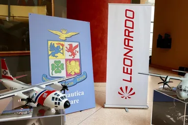 Esposizione dell'azienda aerospaziale Leonardo con modelli di aeromobili, branding e materiali espositivi, che rappresentano l'industria della difesa e dell'aviazione