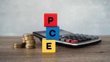 Stacked wooden blocks spelling “PCE” beside a calculator and coins, illustrating the US Personal Consumption Expenditures inflation index.
