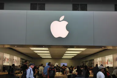 Apple logo displayed above the entrance of an Apple Store with customers browsing inside.