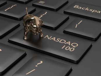 A key on a computer keyboard adapted to say NASDAQ 100, with a small gold bull charm sitting on it 
