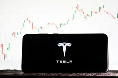 Bild des Tesla-Logos auf einem Smartphone vor dem Hintergrund von Börsentrends