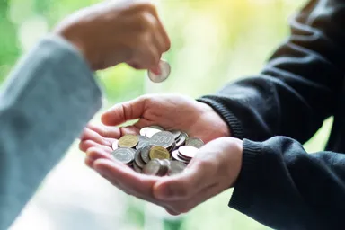 一隻手正把硬幣放入另一人捧著、裝滿零錢的雙手中。