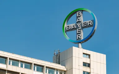 Bayer company logo mounted on top of a modern office building against a clear blue sky.