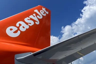 EasyJet aircraft tail and wing against a blue sky with white clouds.