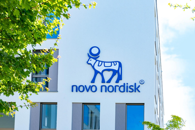 Novo Nordisk Logo an der Außenwand eines modernen Bürogebäudes mit grünen Bäumen im Vordergrund