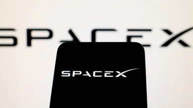 SpaceX-Logo auf einem Smartphone-Bildschirm mit verschwommenem SpaceX-Logo im Hintergrund