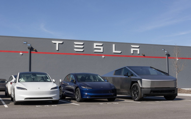 Véhicules Tesla stationnés devant un bâtiment de l'entreprise avec le logo de la société affiché sur le mur sous un ciel bleu dégagé