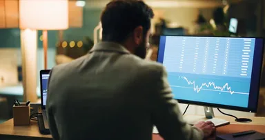 Trader reviewing financial charts and stock market data on a desktop computer