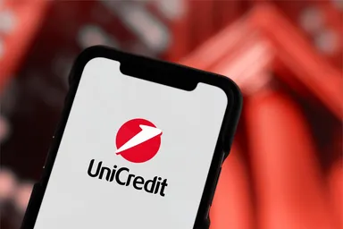 Close-up of a smartphone displaying the UniCredit logo against a blurred red background.