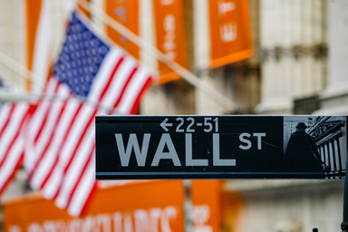 Cartello di Wall Street con bandiera americana sullo sfondo davanti al New York Stock Exchange.