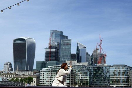 A woman takes a photograph in front of the city of London financial district in London, Britain, May 18, 2022. 