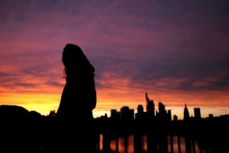 A file photo of a woman wearing a protective mask walks past the skyline of the financial district during sunset in Frankfurt, Germany, October 26, 2020,