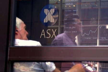 A file photo shows a pedestrian reflected in a window where an investor sits looking at a board displaying stock prices at the Australian Securities Exchange (ASX) in Sydney, Australia February 9, 2018.