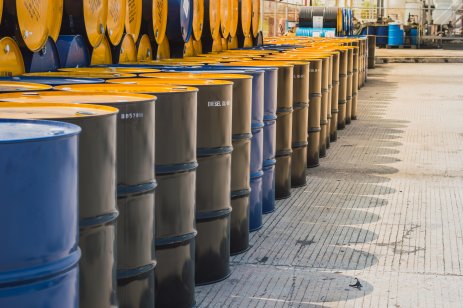 Barrels of oil stand in a row in an industrial yard