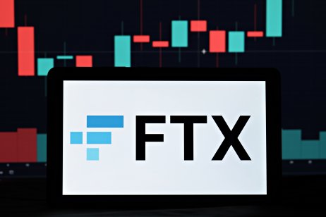 The FTX name and logo on a mobile phone in front of a price graph 
