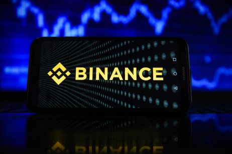 A smartphone displays the Binance logo in front of a blurred stock chart 