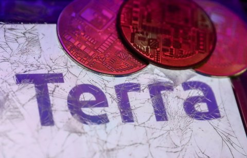 Terra logo displayed on a phone screen is seen through a broken glass with representation of cryptocurrency in this illustration photo